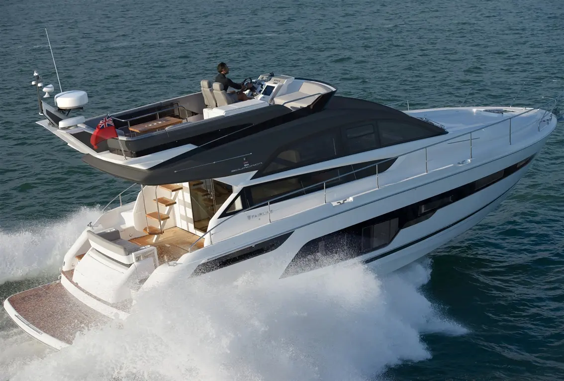 A modern luxury yacht navigates through blue waters, with a captain at the helm and British flag displayed.